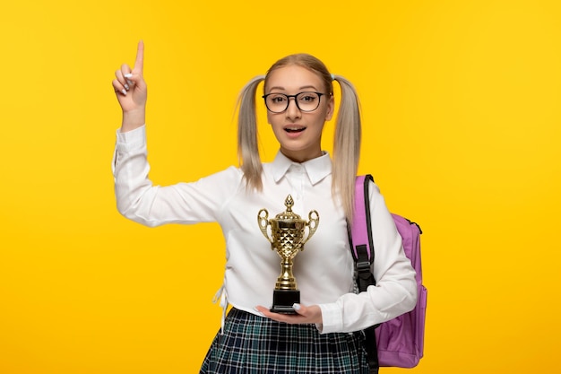 Welttag des Buches aufgeregtes Schulmädchen mit Pferdeschwänzen, die Trophäe auf gelbem Hintergrund halten