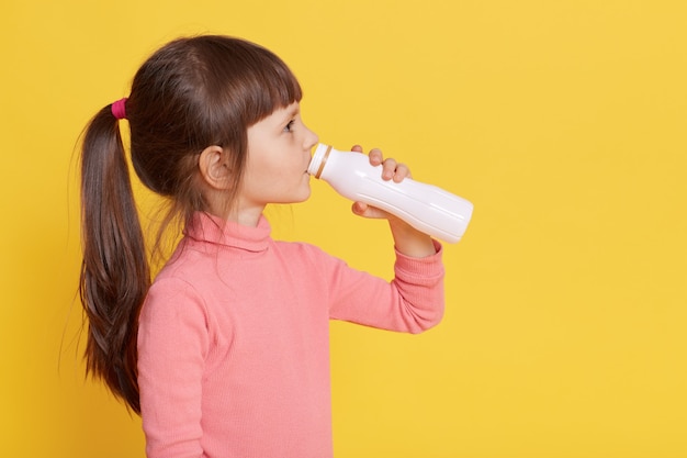 Wenig trinkt Milch, während sie isoliert auf Gelb aufwirft