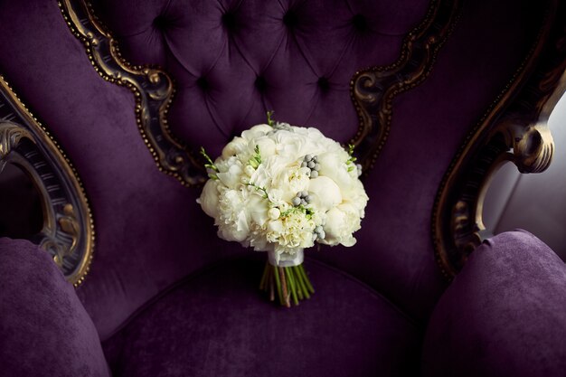 Wenig weißer Hochzeitsblumenstrauß steht auf violettem Stuhl