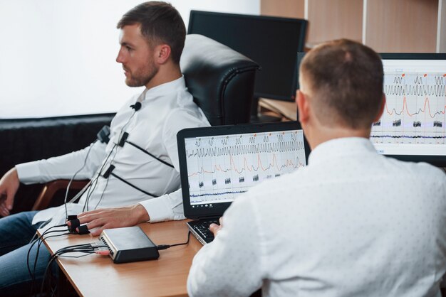 Wer war bei dir, als du das Geld genommen hast? Verdächtiger Mann übergibt Lügendetektor im Büro. Fragen stellen. Polygraphentest