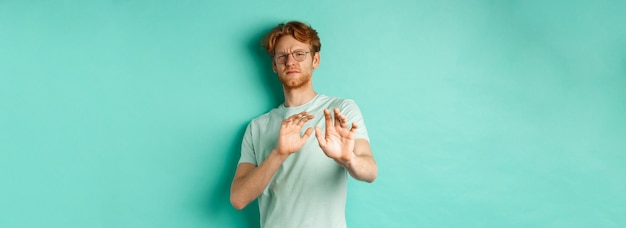 Kostenloses Foto widerstrebender rothaariger mann mit brille, der die hände in einer ablehnenden geste hebt, tritt zurück und vermeidet etwas