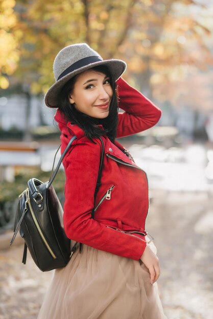 Winsome Frau in der leuchtend roten Jacke, die über Schulter während des Spaziergangs im Herbstpark schaut