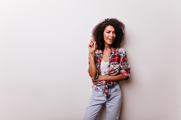 Winsome junge Dame in Blue Jeans, die Innenschuß genießt. Porträt der raffinierten afrikanischen Frau im roten Freizeithemd.