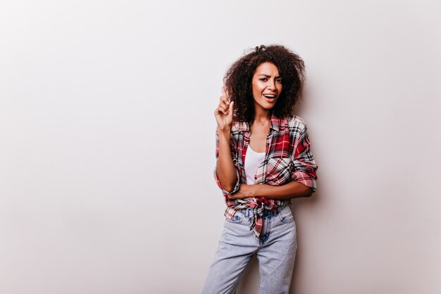 Winsome junge Dame in Blue Jeans, die Innenschuß genießt. Porträt der raffinierten afrikanischen Frau im roten Freizeithemd.