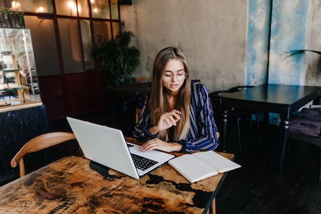 Winsome weibliche Sekretärin, die mit Computer arbeitet. Innenaufnahme des reizenden kaukasischen Studenten, der Laptop für Hausaufgaben verwendet.