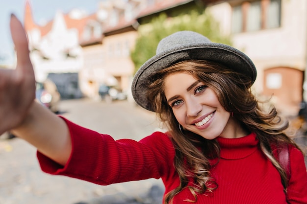 Kostenloses Foto winsome weiße frau im gestrickten pullover, der selfie beim gehen auf allee macht