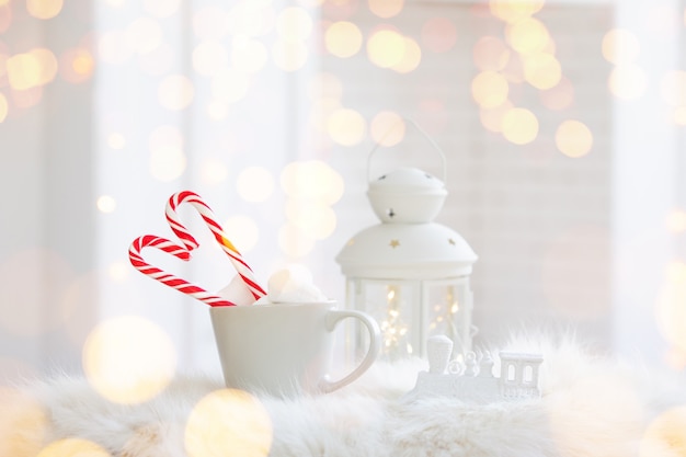 Winterbecher des heißen Getränks mit einer Zuckerstange auf weißem hölzernem Hintergrund