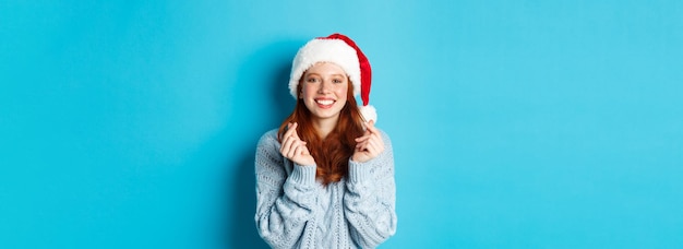 Kostenloses Foto winterferien und heiligabendkonzept hoffnungsvolles rothaariges mädchen in weihnachtsmütze, das wünsche an weihnachten mit macht