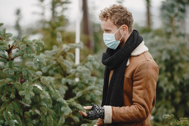 Winterkonzept. Kerl in einem braunen Mantel. Verkäufer des Weihnachtsbaums. Thema Coronavirus.