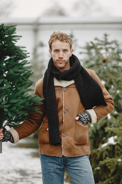 Kostenloses Foto winterkonzept. kerl in einem braunen mantel. verkäufer des weihnachtsbaums.