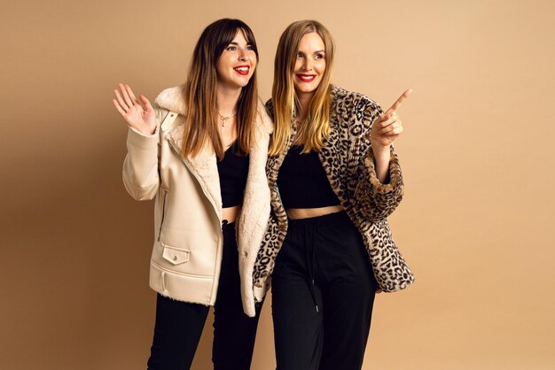 Winterstudio-Porträt von glücklichen zwei stilvollen Frauen, die warme Pelzmäntel tragen, die im beigen Hintergrund-Glamour-Stil posieren