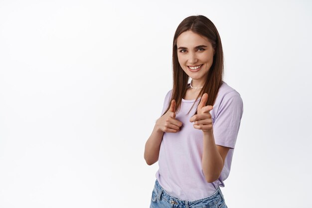 Wir brauchen Sie. Junge selbstbewusste Frau, die mit dem Finger auf die Kamera zeigt, nach Mitarbeitern sucht, Leute rekrutiert, für gute Arbeit lobt und vor weißem Hintergrund steht.