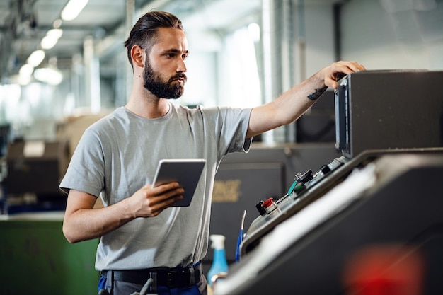 Wirtschaftsingenieur, der eine CNC-Maschine bedient und ein digitales Tablet in einer Fabrik verwendet