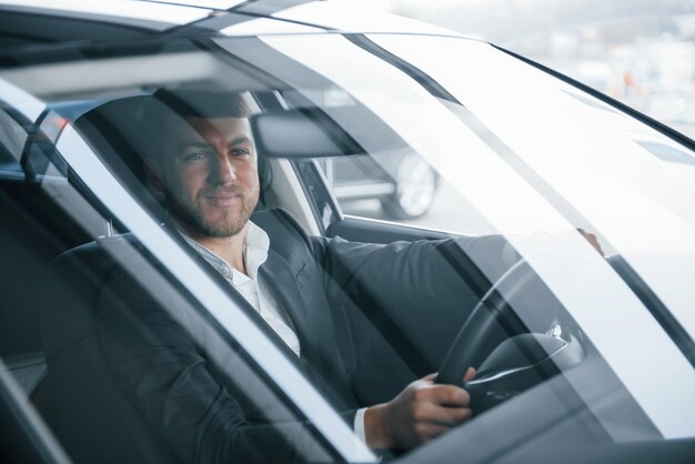 Wo hin. Moderner Geschäftsmann, der sein neues Auto im Autosalon versucht