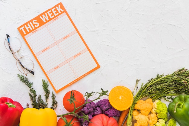 Wöchentlicher Mahlzeitplan mit bunten Obst und Gemüse auf strukturiertem Hintergrund