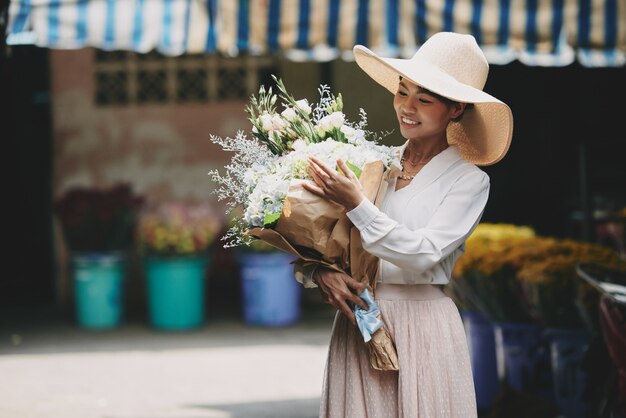 Wohlhabende schicke Asiatin, die den großen Blumenstrauß gekauft am Blumenladen bewundert