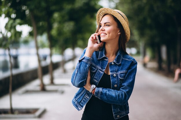 Womanwearing Kleid und Hut draußen im Park mit Telefon