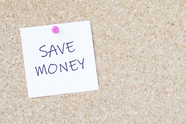 Worte "Geld sparen" auf einem Papier, das mit einer Stecknadel an einer Tafel befestigt ist