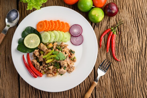 Würziger gehackter Schweinefleischsalat auf einem weißen Teller auf Holztisch.