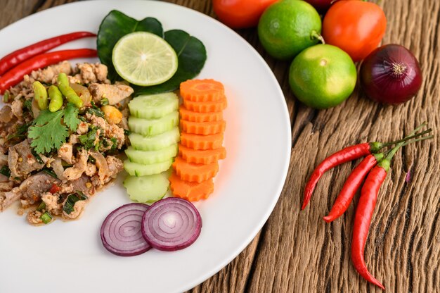 Würziger gehackter Schweinefleischsalat auf einem weißen Teller auf Holztisch.