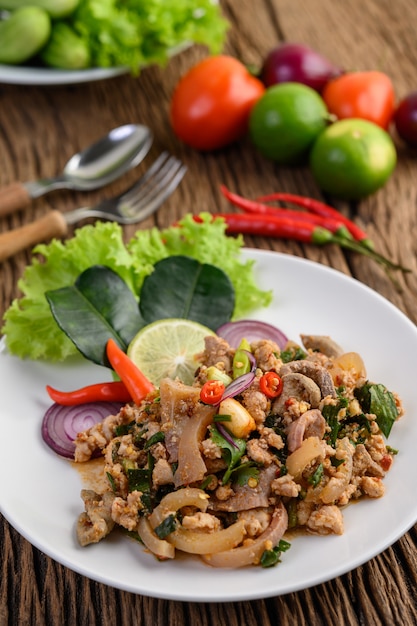 Würziger gehackter Schweinefleischsalat auf einem weißen Teller auf Holztisch.