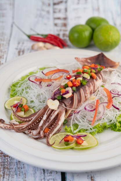 Würziger Zitronenkalmar mit Galangal, Chilis, Karotten, Pfefferminze, Frühlingszwiebeln und Knoblauch auf einem Teller auf weißem Holzboden.