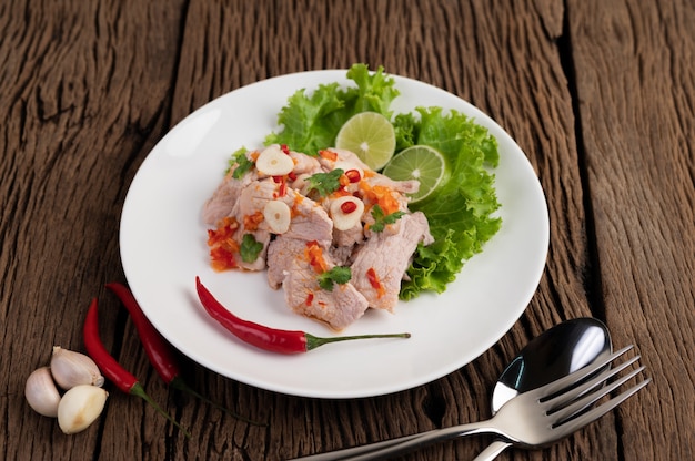 Würziges Limettenschweinefleisch mit Salat, Galangal, Chili, Tomate und Knoblauch auf einem weißen Teller auf einem Holzboden.