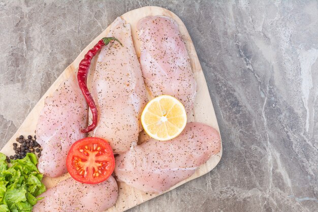 Würziges rohes Hühnerfleisch und Gemüse auf einem Schneidebrett auf dem Marmor.