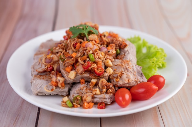 Würziges Schweinefleisch mit Tomaten und Salat auf einem weißen Teller auf einem Holztisch gehackt.