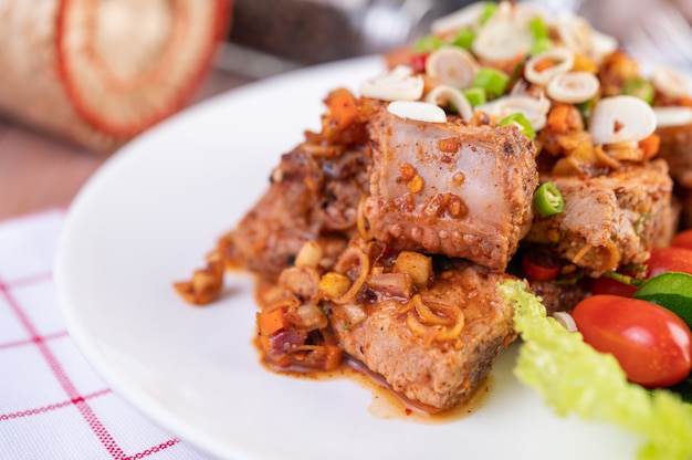 Würziges Schweinefleisch mit Tomaten und Salat auf einem weißen Teller auf einem Holztisch gehackt.