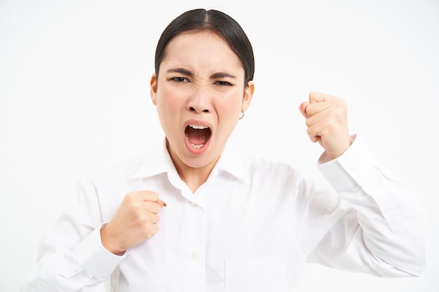 Wütende asiatische Frau schreit und schüttelt die Fäuste und schreit Mitarbeiter an, die frustriert vor weißem Hintergrund stehen