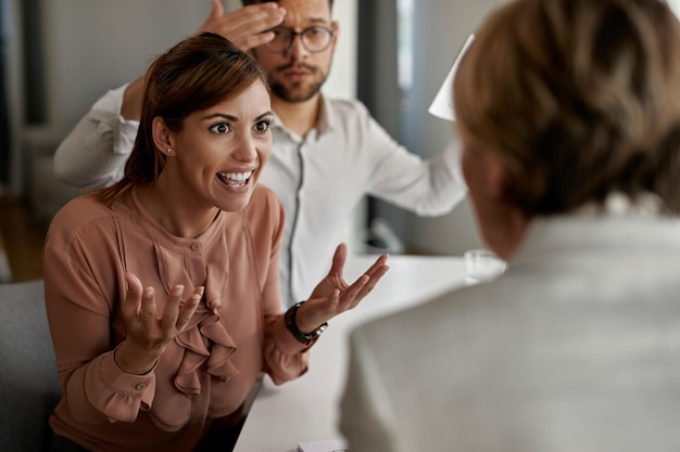 Wütende Frau, die ihren Immobilienmakler anschreit, während sie ein Meeting im Büro hat