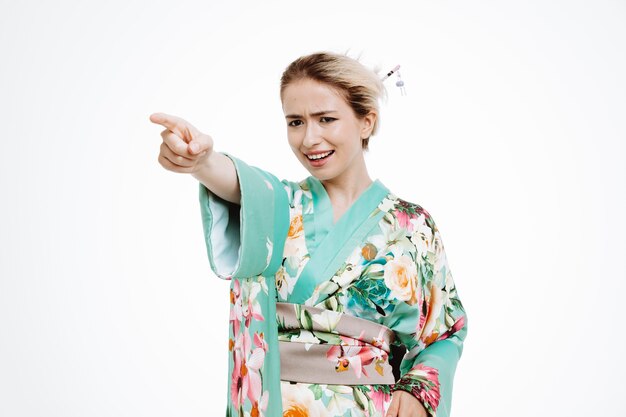 Wütende Frau im traditionellen japanischen Kimono zeigt mit dem Zeigefinger zur Seite auf Weiß