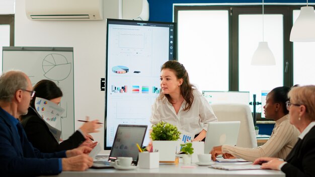 Wütende Managerin, die Mitarbeiter für schlechtes Arbeitsergebnis argumentiert, Konferenzraum sitzt, verschiedene Kollegen, die verängstigt aussehen. Geschäftsfrau, die über Multitasking-Schwierigkeiten tobt und im Sitzungssaal schreit