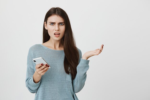 Wütende verwirrte Frau, die sich beschwert und Smartphone hält