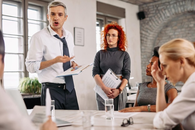 Wütender Geschäftsmann, der sich von Geschäftsberichten enttäuscht fühlt und sein Team während eines Meetings im Büro schimpft