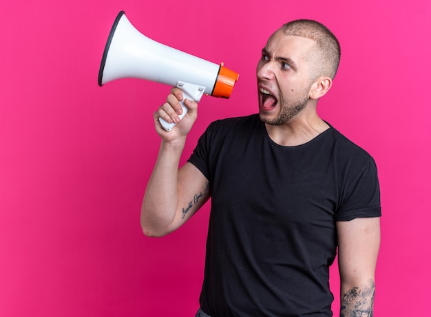 Wütender junger gutaussehender Kerl mit schwarzem T-Shirt spricht über Lautsprecher isoliert auf rosa Wand