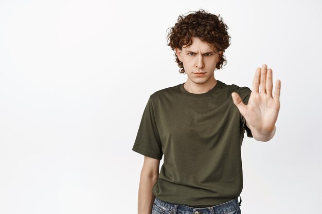 Wütender junger Teenager streckt die Hand aus und zeigt Stopp-Verweigerungsgeste verbietet etw, ernst vor weißem Hintergrund zu stehen