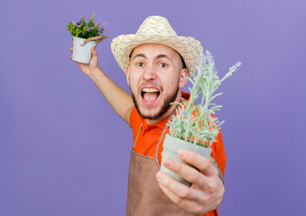 Wütender männlicher Gärtner mit Gartenhut hält Blumentöpfe