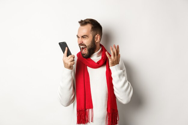 Wütender Mann schreit Smartphone mit wütendem Gesicht an und steht wütend vor weißem Hintergrund