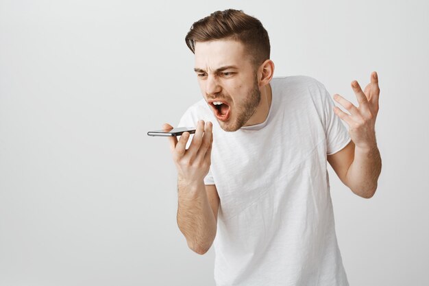 Wütender verärgerter Kerl, der den mobilen Lautsprecher anschreit, wütende Sprachnachricht aufzeichnen