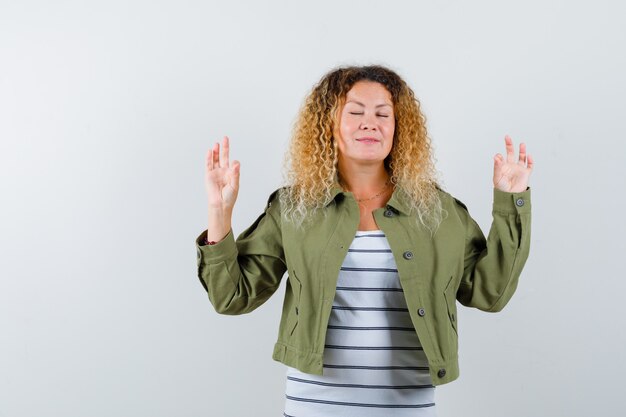 Wunderbare Frau, die Meditationsgeste in der grünen Jacke, im Hemd zeigt und friedlich aussieht. Vorderansicht.