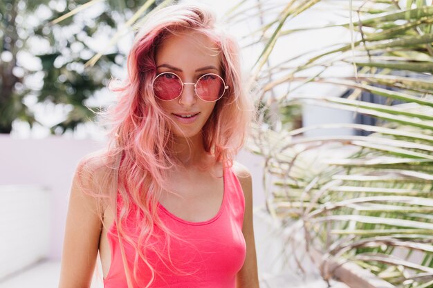 Wunderbare junge Frau im stilvollen Sommeroutfit, das auf exotischem Hintergrund aufwirft.