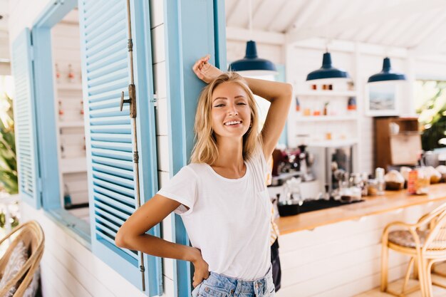 Wunderbare leicht gebräunte Frau in Retro-Jeans, die mit positivem Lächeln aufwirft.