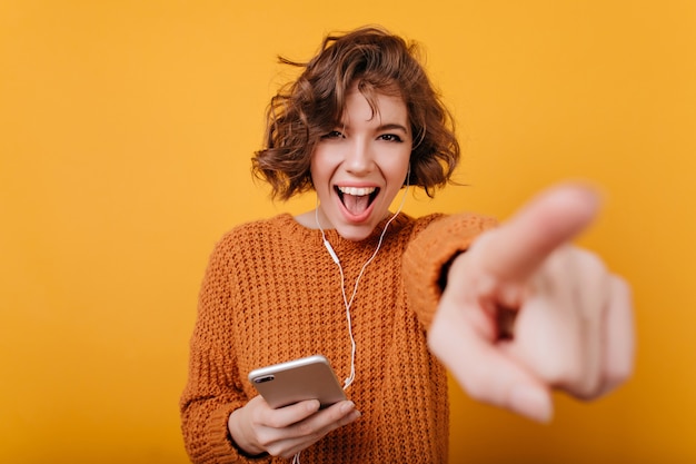 Wunderbares Mädchen mit braunem Haar, das Telefon und Zeigefinger hält