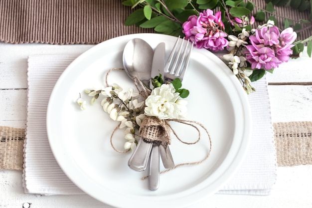 Wunderschön elegant dekorierter Tisch für den Urlaub mit Frühlingsblumen und -grün - Hochzeit oder Valentinstag mit modernem Besteck, Bogen, Glas, Kerze und Geschenk, horizontal, Nahaufnahme, getönt