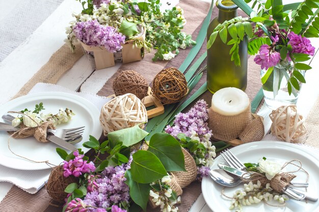 Wunderschön elegant dekorierter Tisch für den Urlaub mit Frühlingsblumen und Grüns - Hochzeit oder Valentinstag mit modernem Besteck, Schleife, Glas, Kerze und Geschenk, horizontal, Nahaufnahme, getönt