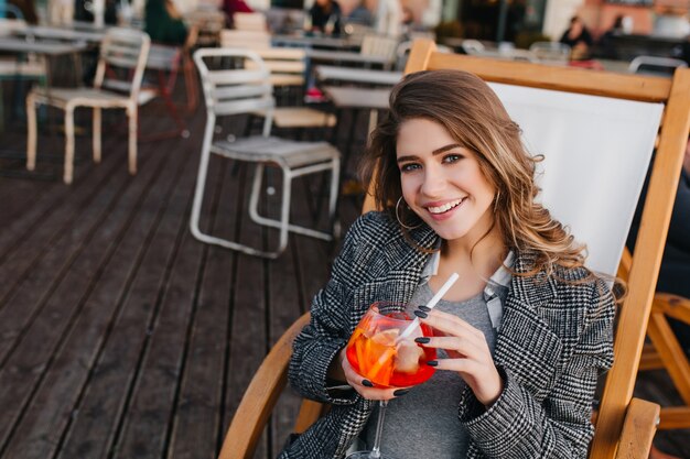 Wunderschöne blasse Dame in guter Laune, die Orangencocktail im Straßencafé schmeckt