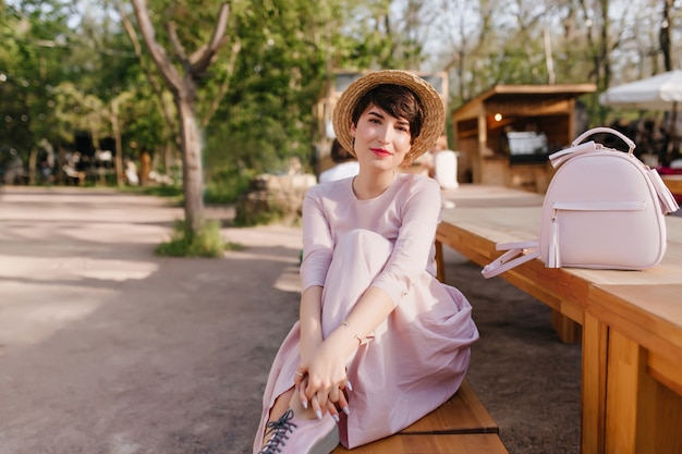 Wunderschöne Dame mit trendiger Frisur, die auf Bank ruht und ihr Bein umarmt