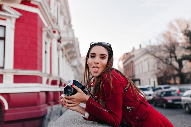 Wunderschöne europäische Dame, die mit Zunge heraus beim Gehen durch Stadt mit Kamera aufwirft